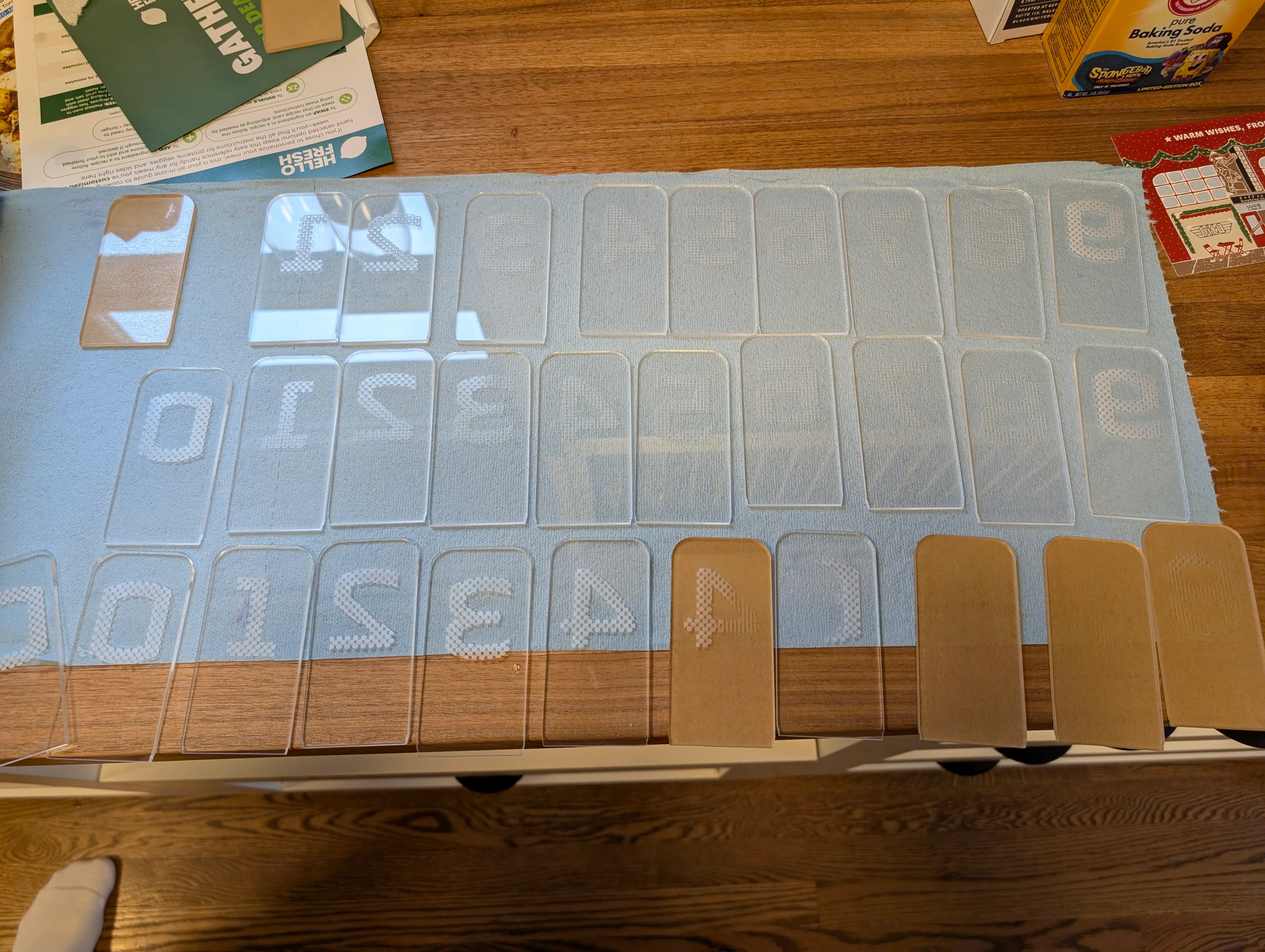 A sheet of laser-engraved clear acrylic panels, each carrying one digit, laid out before assembly