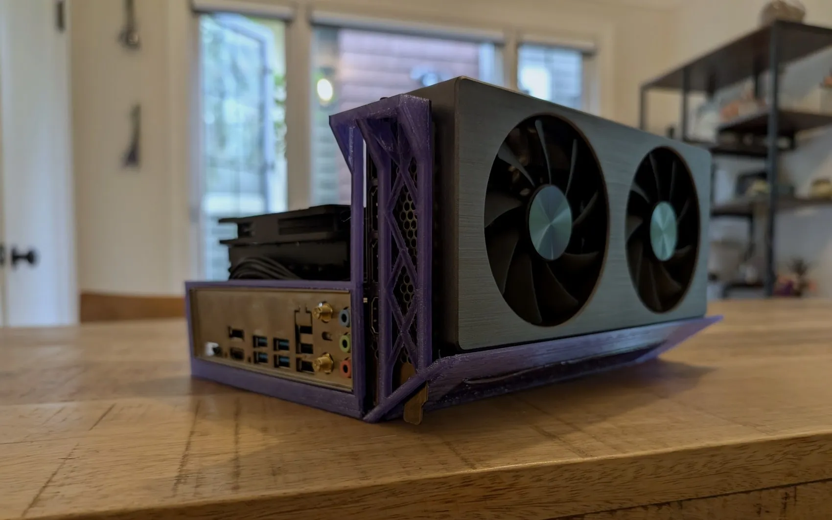 The finished small-form-factor PC in its purple 3D-printed case, graphics card fans facing out, on a wood table